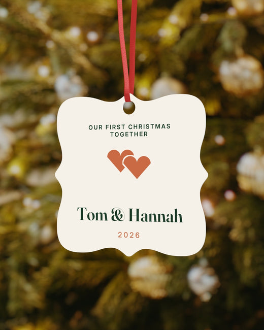 Our First Christmas Together ornament with two hearts and the example names Tom and Hannah, hanging on a Christmas tree