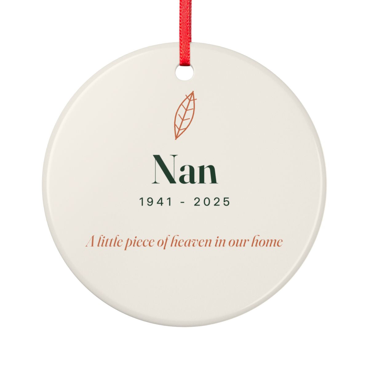 Round ceramic Christmas ornament on a red ribbon with a feather, the name Nan, the years 1941 to 2025 and the line A little piece of heaven in our home