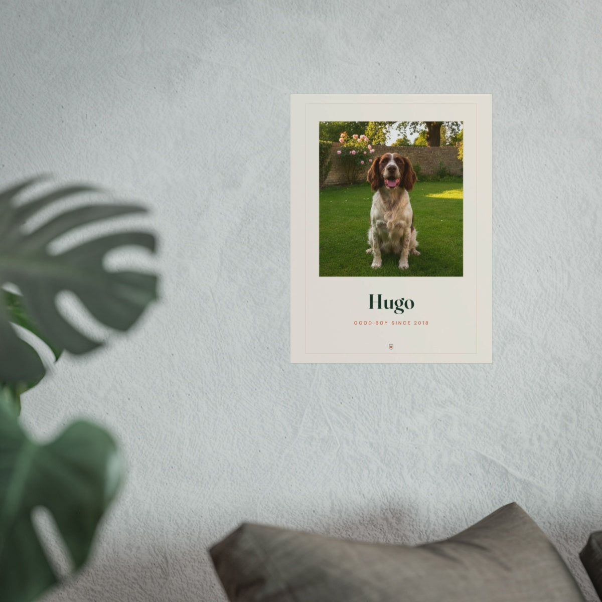Pet photo print mock-up in the larger size on a grey wall above a sofa cushion, with a monstera leaf in front