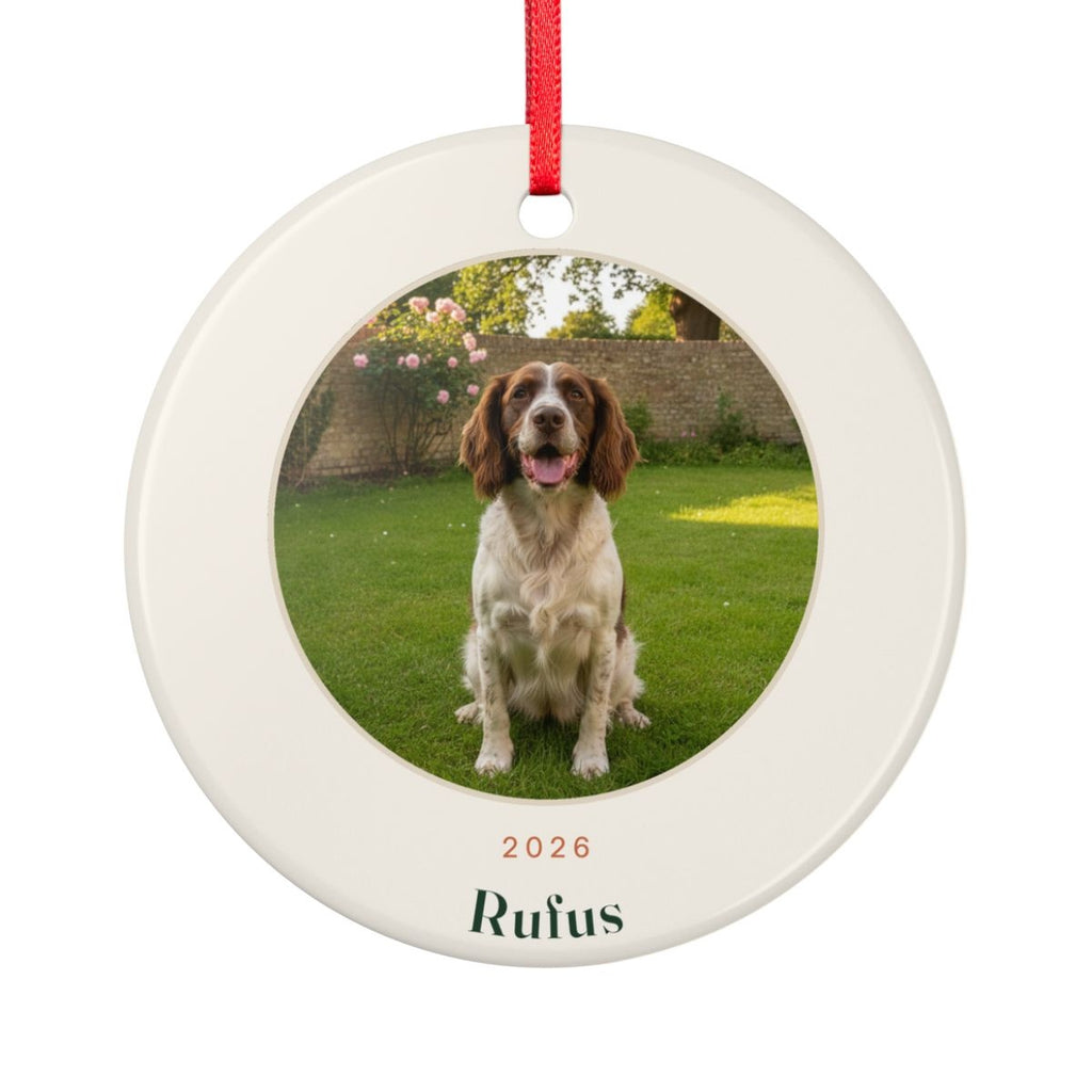 Pet photo ceramic Christmas ornament mock-up seen from the other side, with the same sample spaniel photo, '2026' and 'Rufus', on a red ribbon