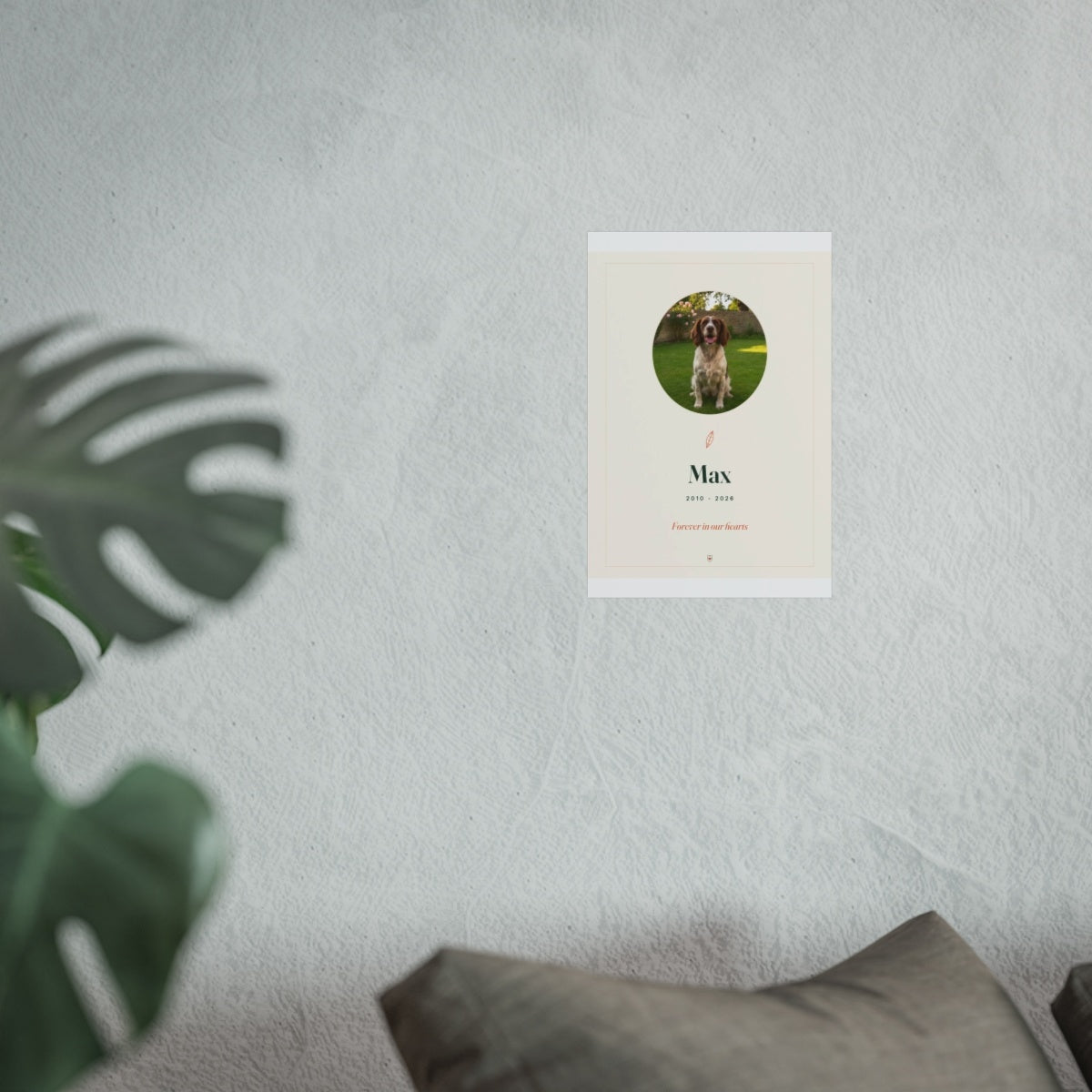 Pet memorial print mock-up shown smaller on the pale wall above the grey sofa, monstera leaf in front