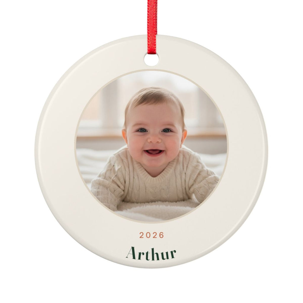 Baby's First Christmas photo ornament mock-up, round ceramic with a red ribbon, a baby's photo, '2026' and 'Arthur'