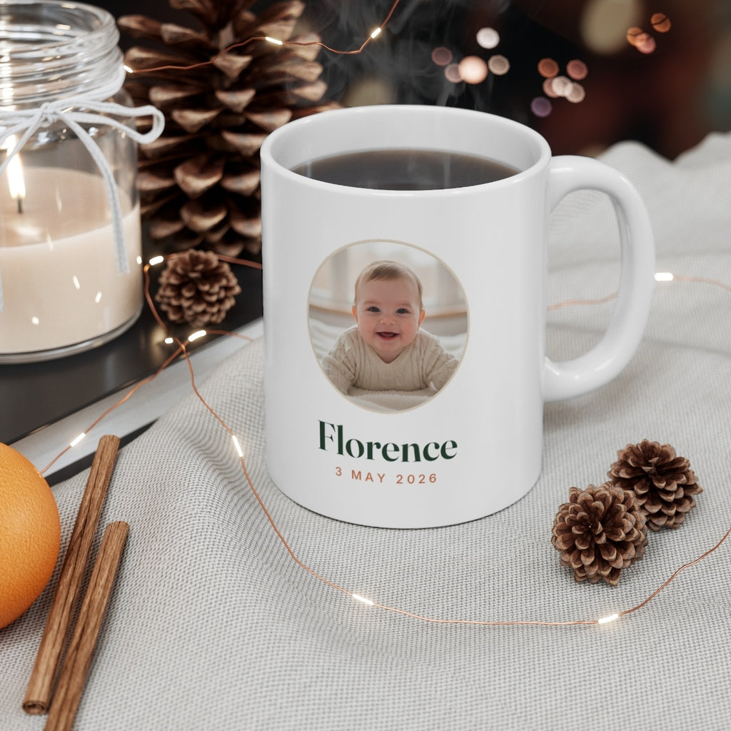 Baby photo mug mock-up filled with coffee beside a candle, pine cones and fairy lights, 'Florence' and '3 May 2026'
