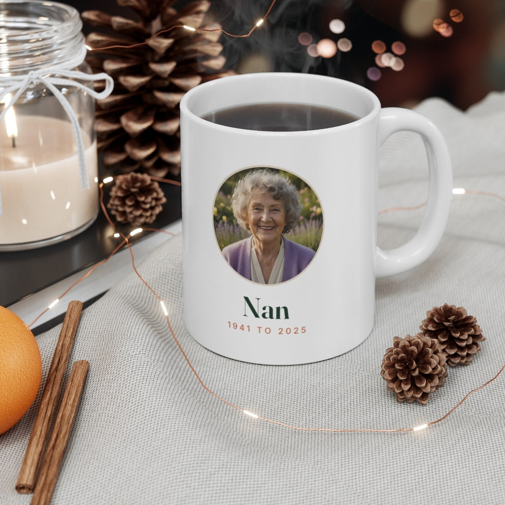 In Loving Memory photo mug mock-up with a hot drink beside a candle and pine cones, sample photo, 'Nan' and '1941 to 2025'