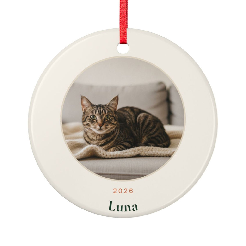 Personalised cat photo ceramic Christmas ornament mock-up on a red ribbon, with a tabby cat's photo, '2026' and 'Luna'