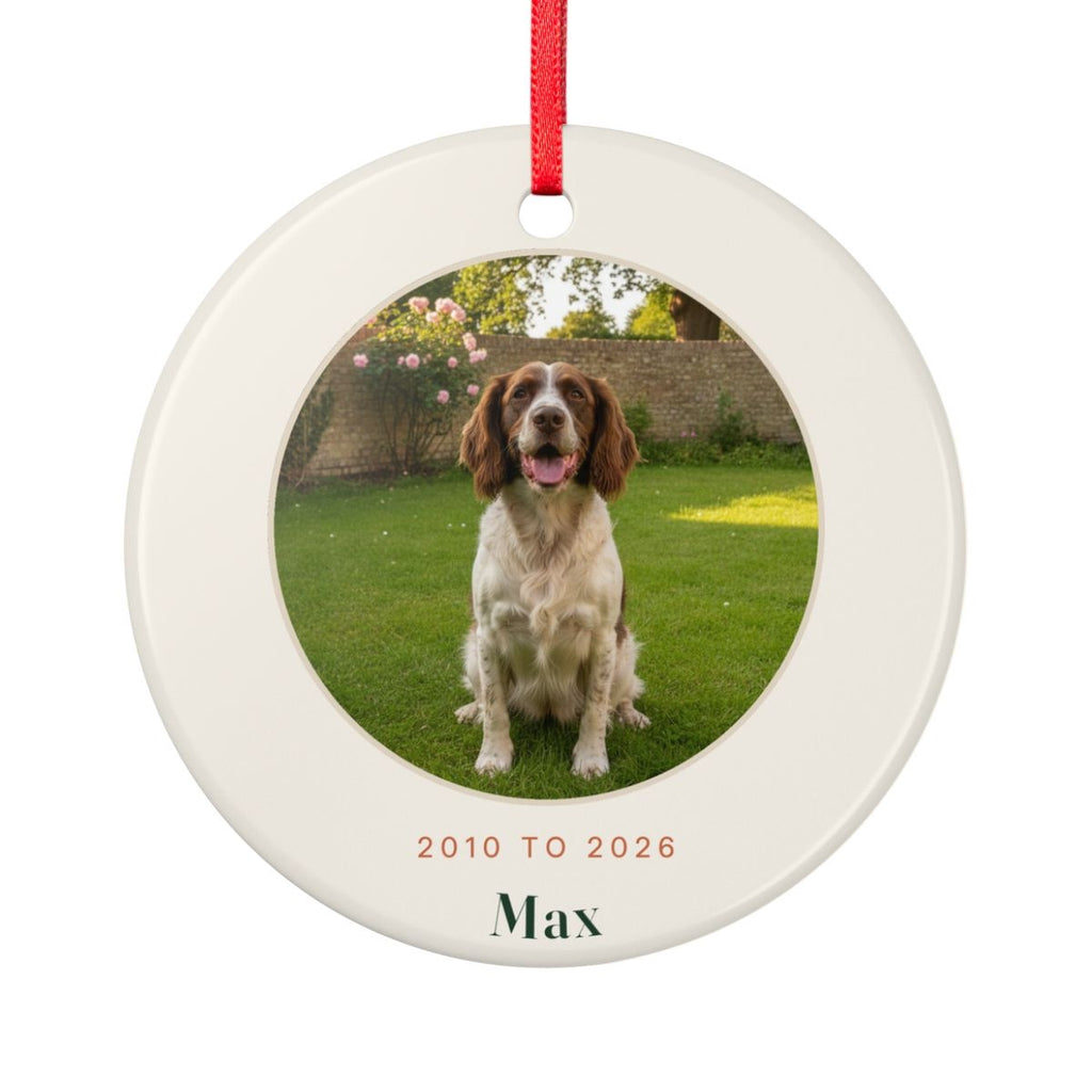 Pet memorial photo ceramic Christmas ornament mock-up with a sample spaniel photo, '2010 to 2026' and 'Max', on a red ribbon