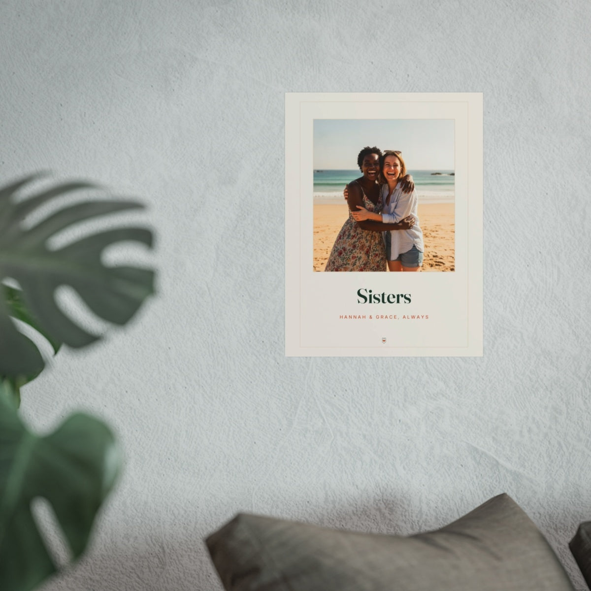 Sisters photo print mock-up hung on a pale wall beside a monstera plant and a grey sofa, shown at the larger size
