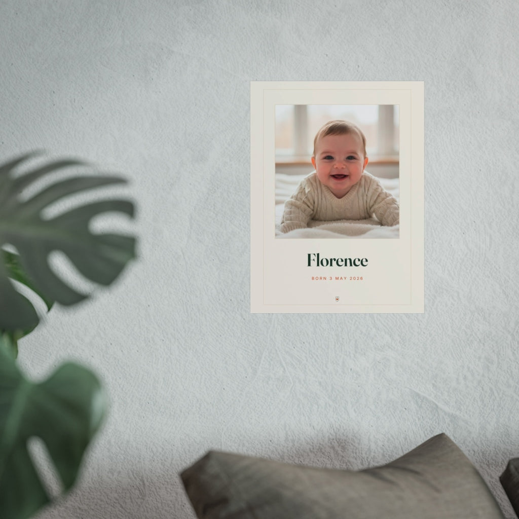 Baby photo print mock-up hung on a pale wall beside a monstera plant and a grey sofa, shown at the larger size