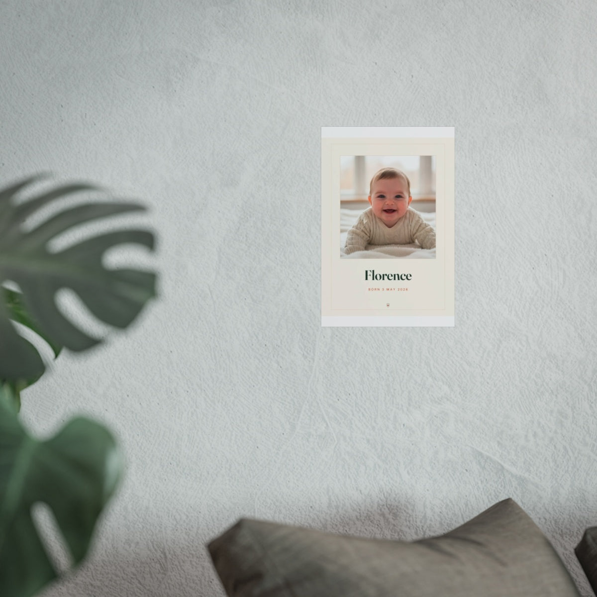 Baby photo print mock-up at the smaller size on a pale wall beside a monstera plant and a grey sofa
