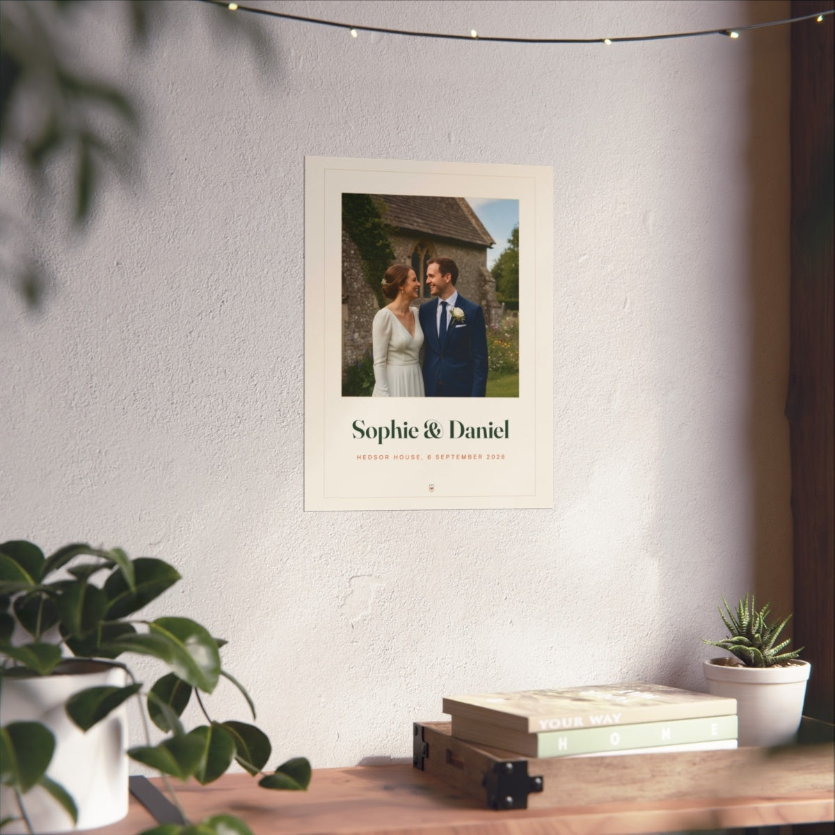 Wedding photo print mock-up on a white wall above a wooden desk with books and a small potted plant