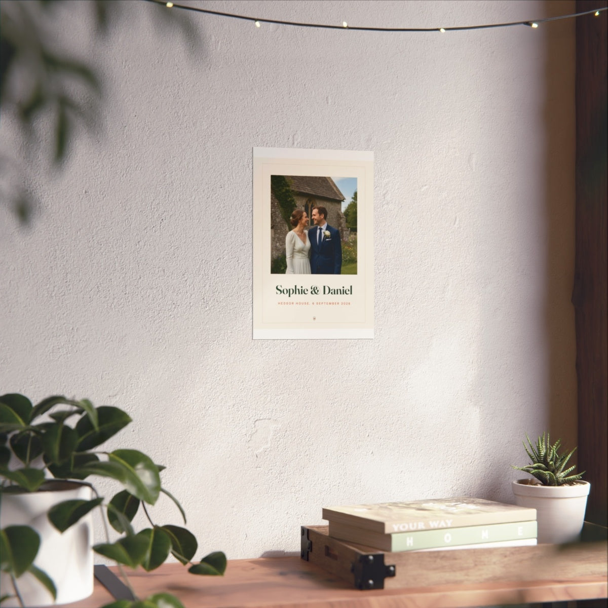 Wedding photo print mock-up shown smaller on the white wall above the desk with books and a plant