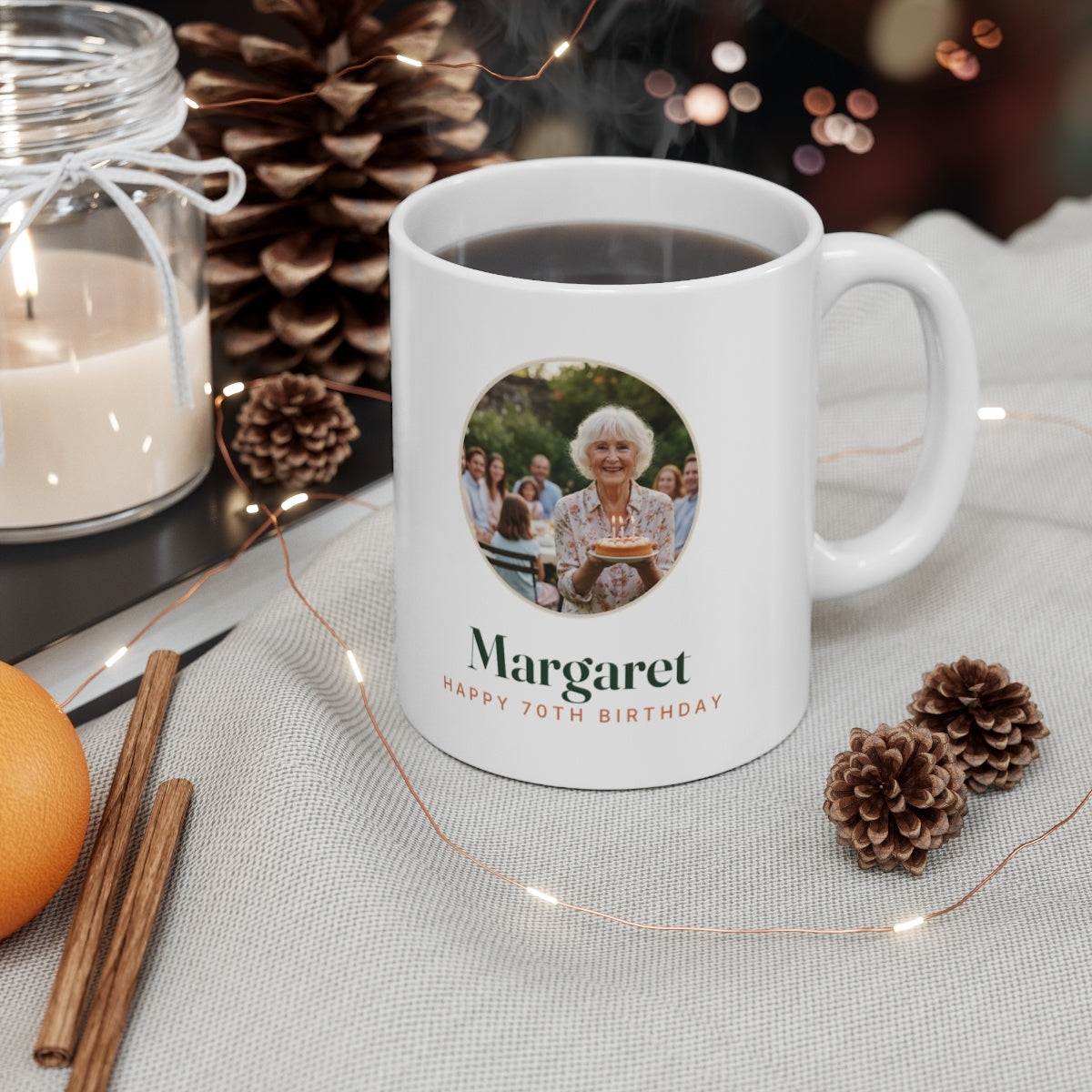 Birthday photo mug mock-up with a hot drink beside pine cones, round sample photo and 'Margaret, Happy 70th Birthday'
