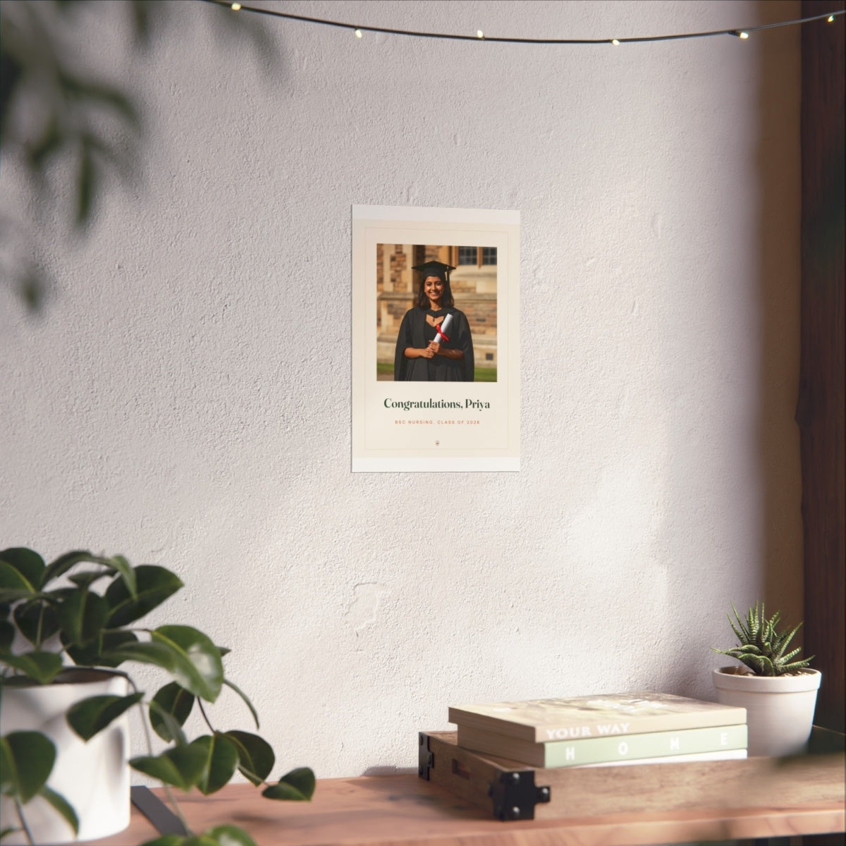 Personalised graduation photo print mock-up at the smaller size on a white wall under string lights above a desk with books