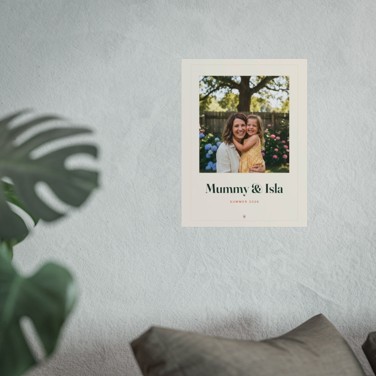 Personalised Mum photo print mock-up on a pale textured wall above grey sofa cushions, with a monstera leaf in front