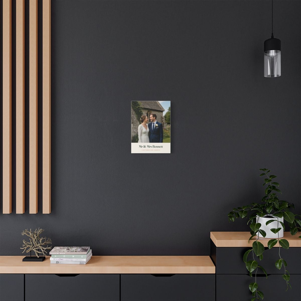 Personalised wedding photo canvas mock-up shown small on a dark grey wall above a sideboard with a trailing plant