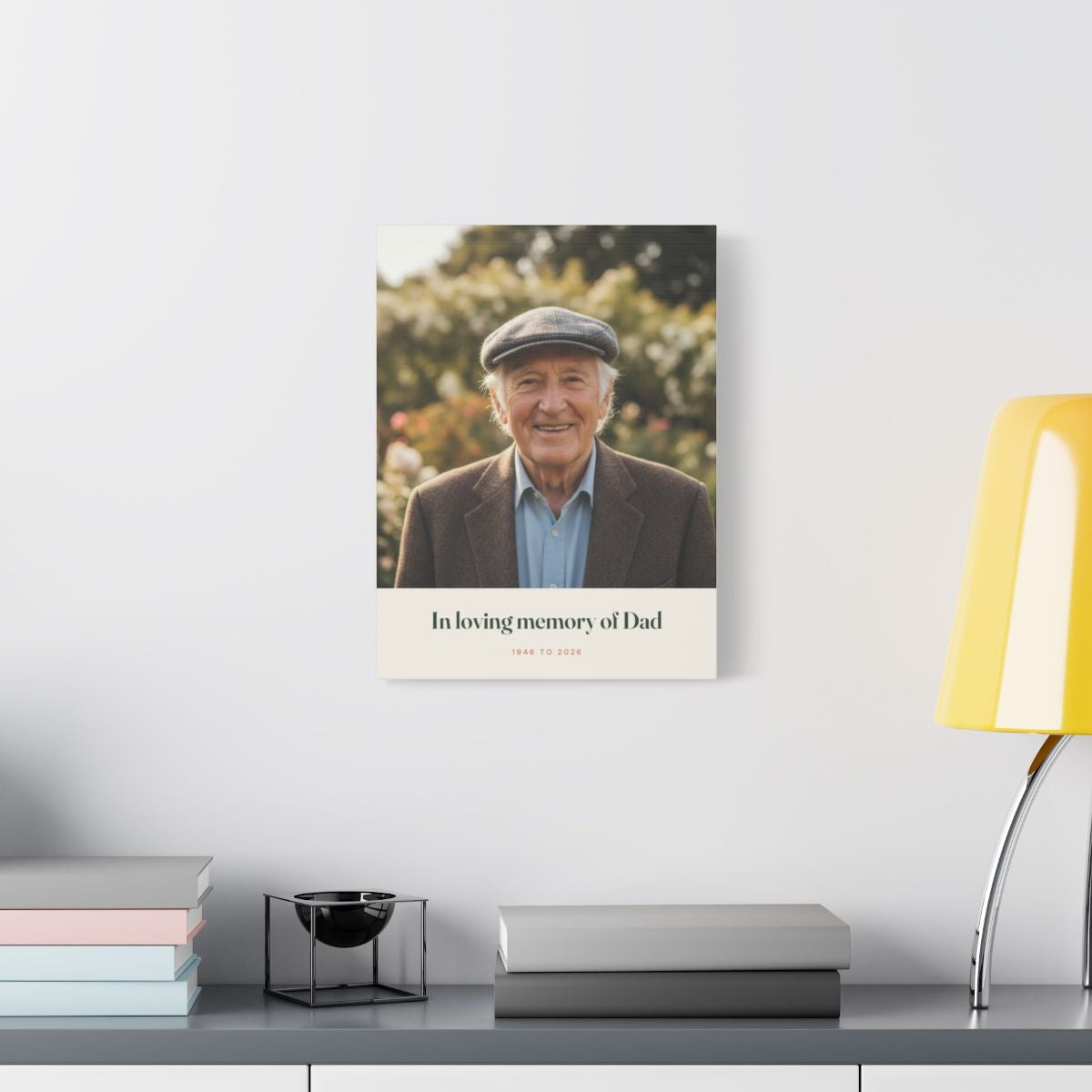 Personalised in loving memory photo canvas mock-up hung on a white wall above a shelf with books and a yellow lamp