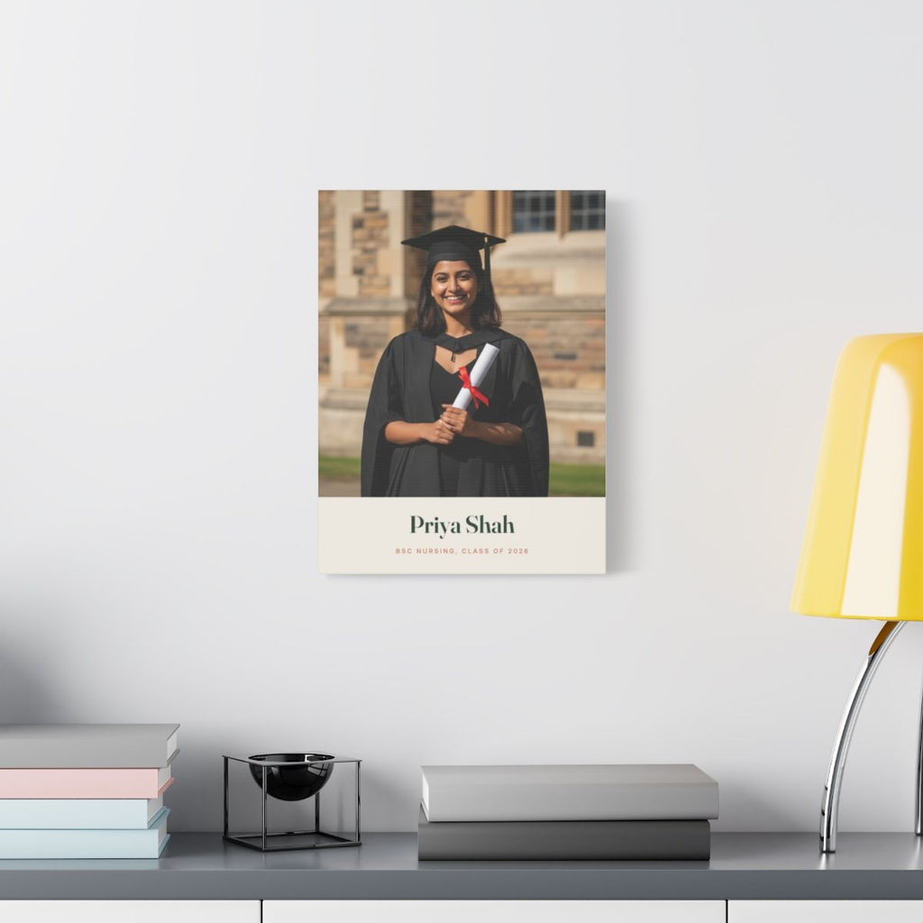 Personalised graduation photo canvas mock-up on a white wall above a desk with books and a yellow lamp