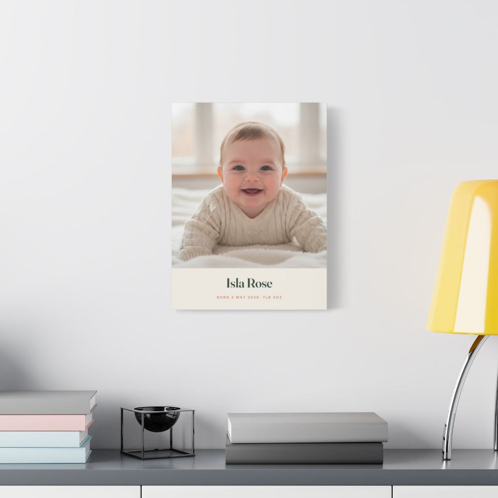 Personalised new baby photo canvas mock-up hung on a pale wall above a desk with books and a yellow lamp