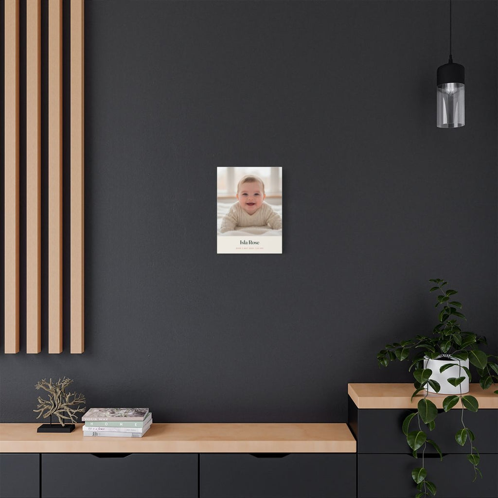 Personalised new baby photo canvas mock-up on a dark grey wall above a sideboard with a trailing plant and wooden slat panel