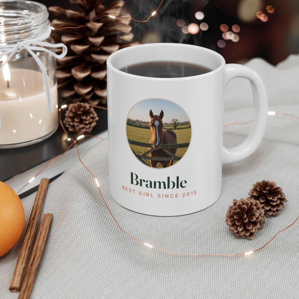 Personalised horse photo mug mock-up filled with coffee on a table beside a candle, pine cones and fairy lights