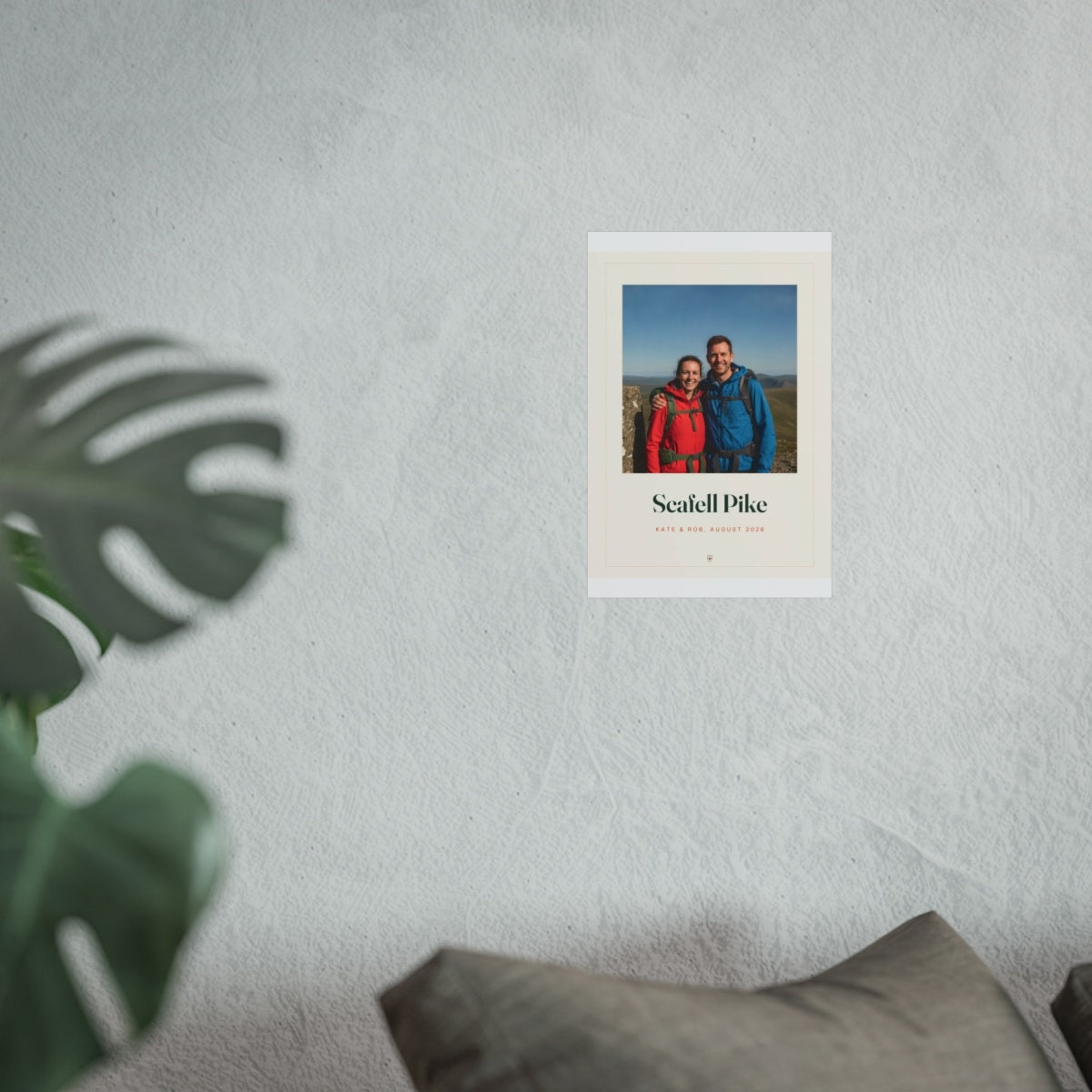 Personalised walking photo print mock-up shown smaller on the pale wall above the grey sofa, monstera leaf in front