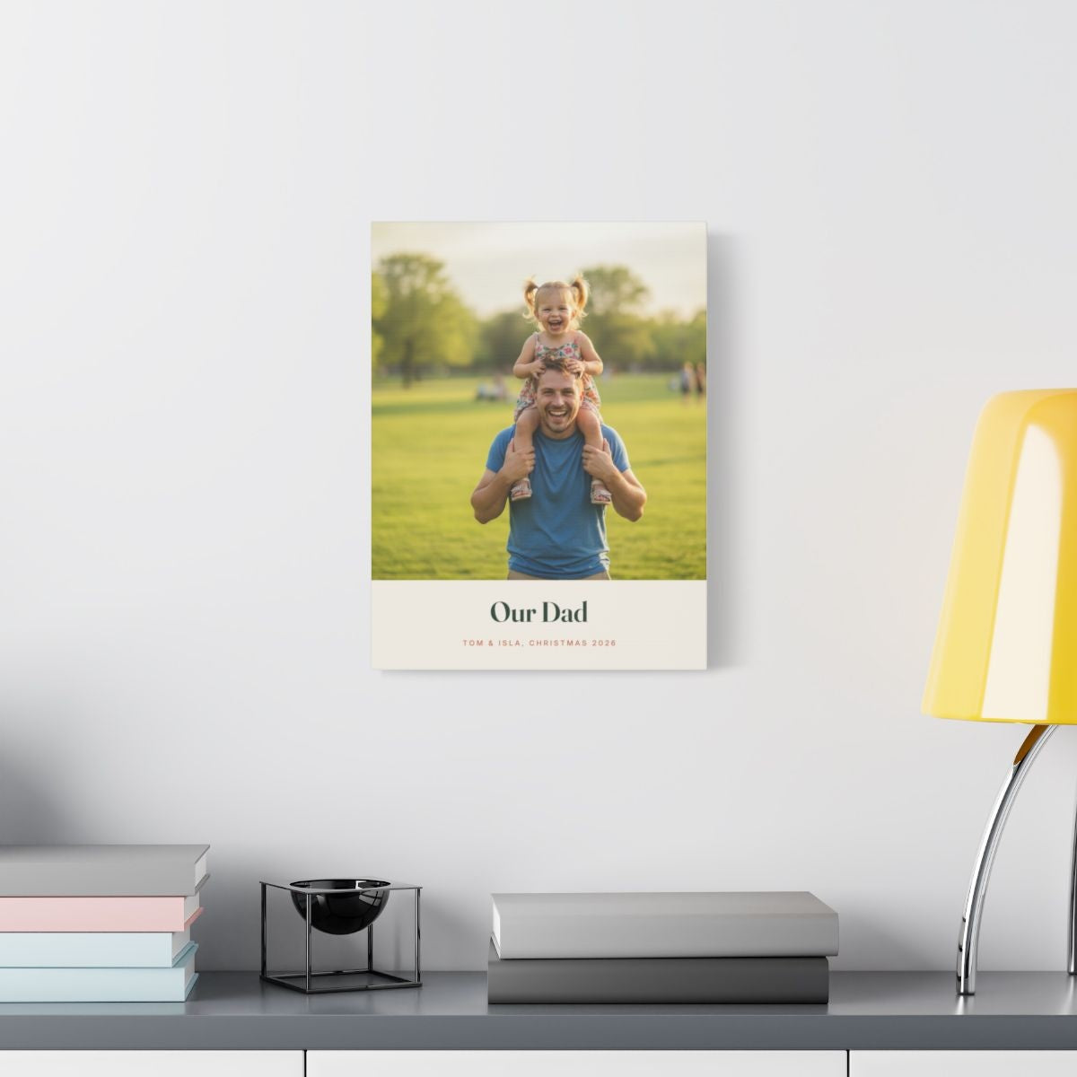 Personalised Dad photo canvas mock-up on a white wall above a desk with books and a yellow lamp