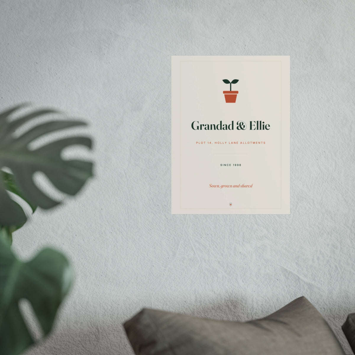 Allotment print mock-up hung on a pale wall beside a monstera plant and a grey sofa, shown at the larger size