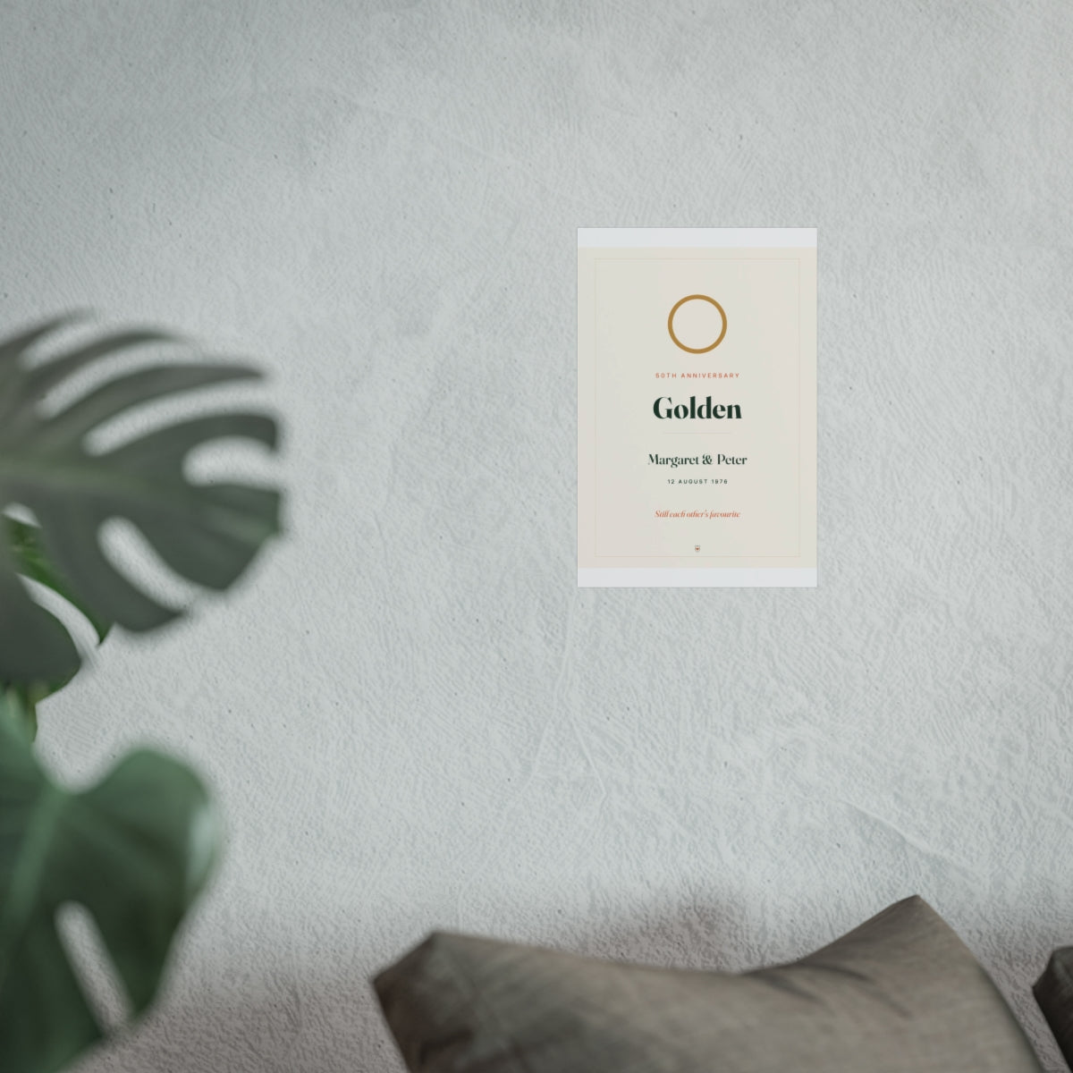 Anniversary print mock-up at the smaller size on a pale wall beside a monstera plant and a grey sofa