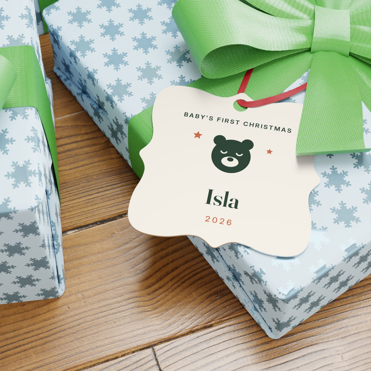 Baby's First Christmas aluminium ornament mock-up on a wrapped gift with a green bow, bear face and sample name 'Isla'