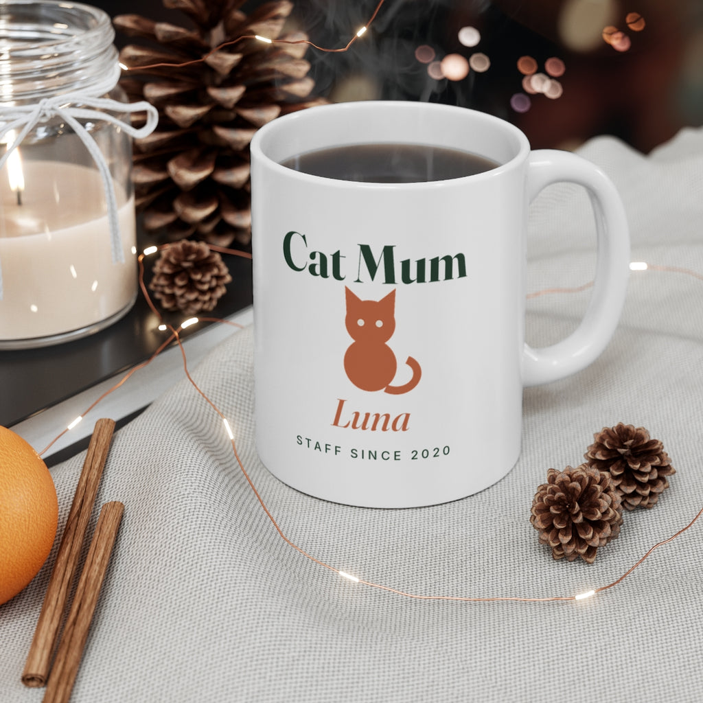 Cat Mum mug mock-up with a hot drink beside a candle, pine cones and fairy lights, printed 'Luna' and 'Staff since 2020'