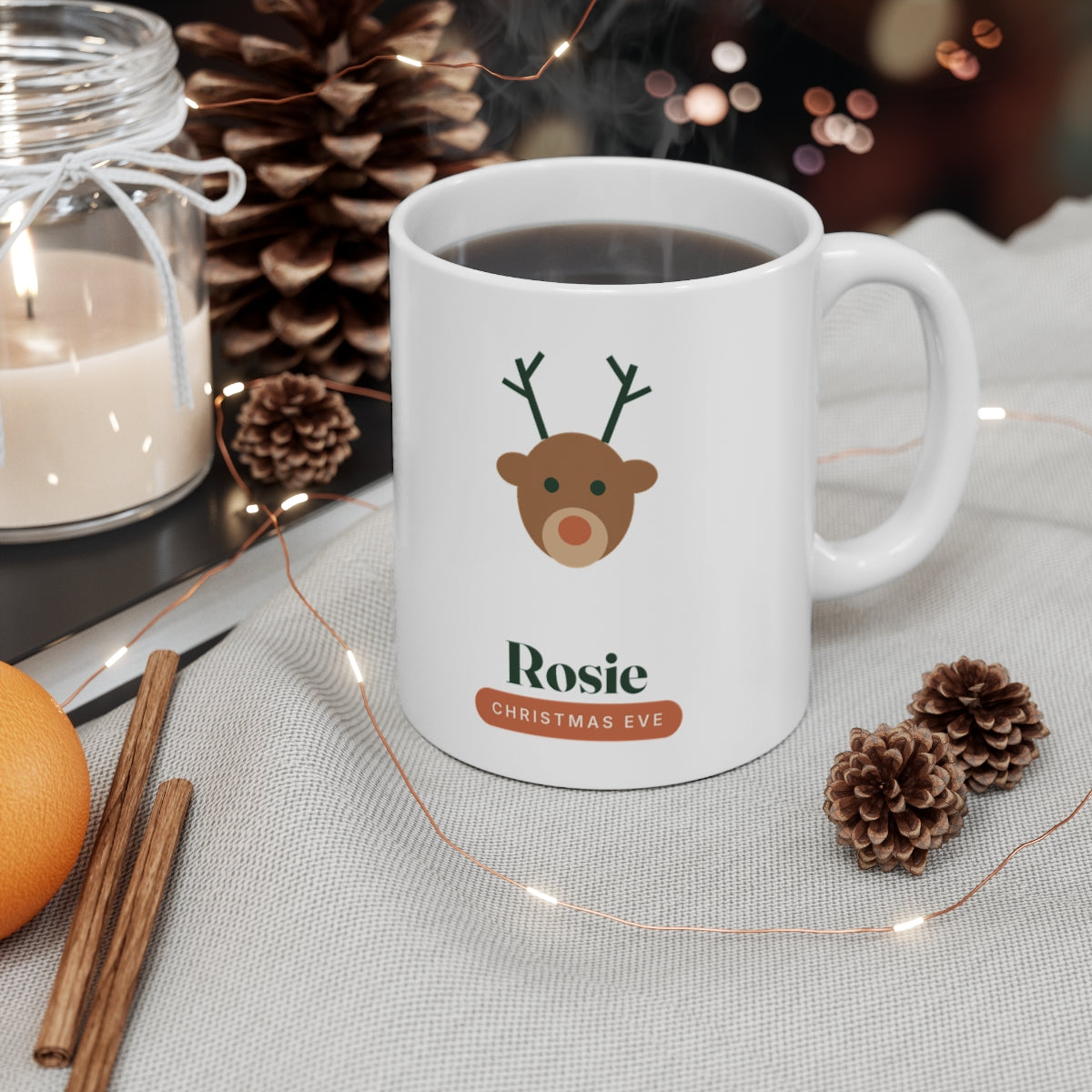 Children's Christmas Eve mug mock-up with a hot drink by a candle, pine cones and fairy lights, a reindeer and 'Rosie'
