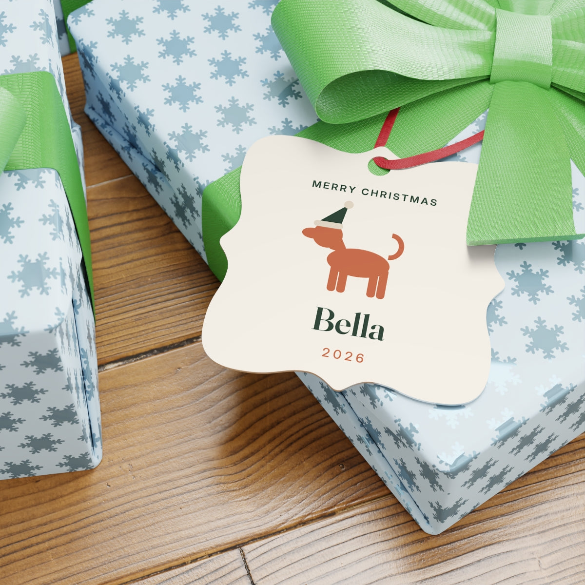 Dog aluminium Christmas ornament mock-up lying on wrapped presents with green bows, 'Merry Christmas' and 'Bella' visible