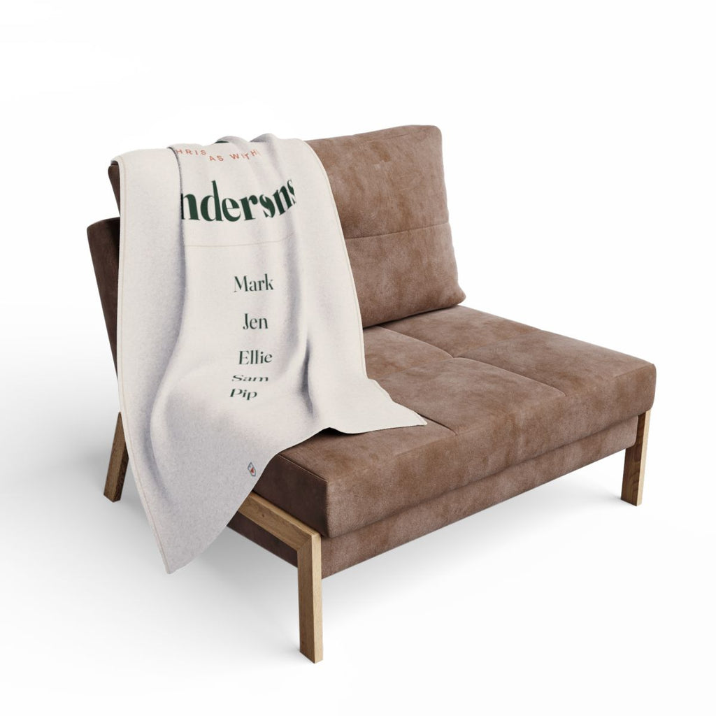 Family Christmas fleece blanket mock-up draped over a brown armchair, 'Andersons' and the five names visible