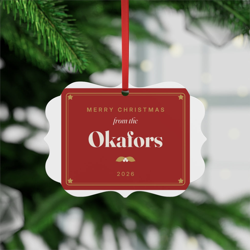 Family aluminium plaque ornament mock-up hanging by its red ribbon on a tree, 'Merry Christmas from the Okafors', '2026'