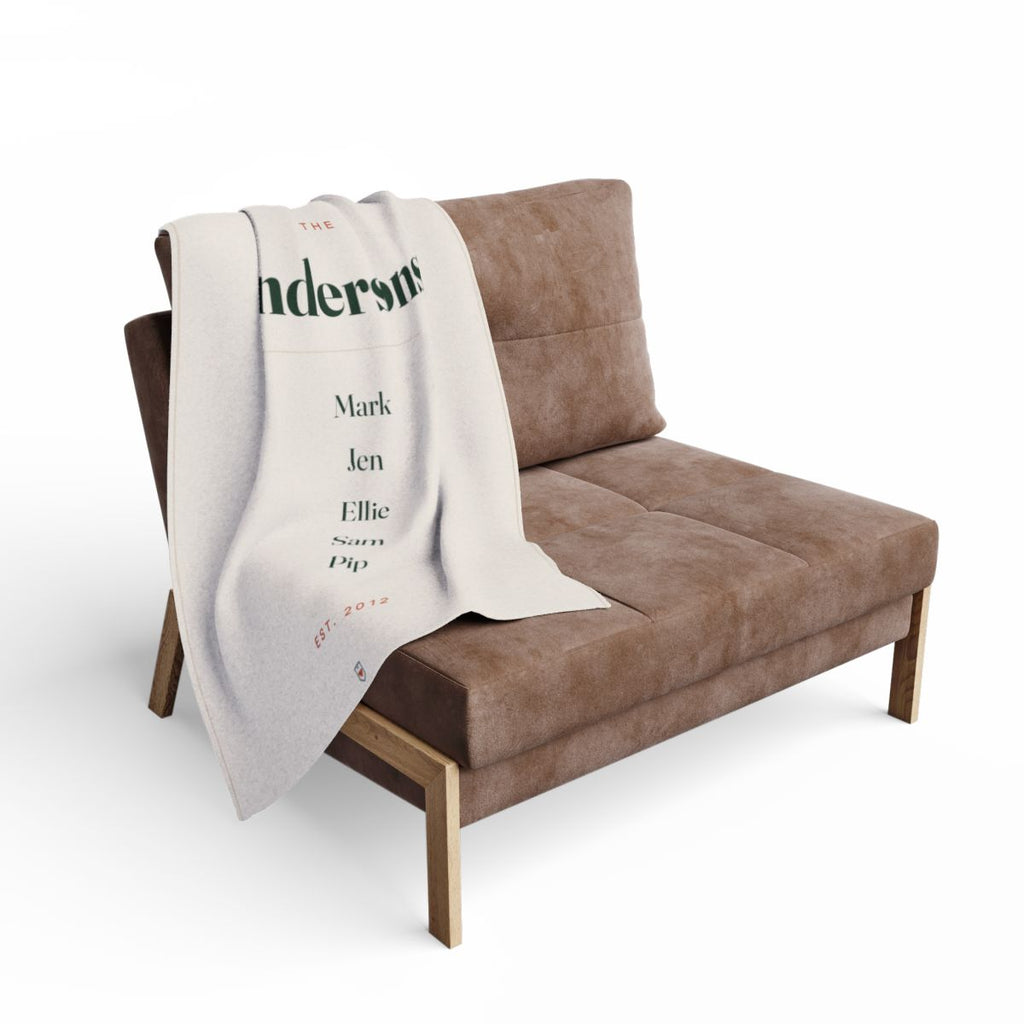 Personalised family name fleece blanket mock-up draped over a brown armchair, showing 'Andersons' and the five names
