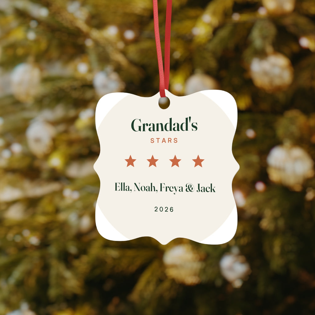 Grandad's Stars ornament mock-up hanging by its red cord on a Christmas tree, printed 'Ella, Noah, Freya & Jack' and '2026'