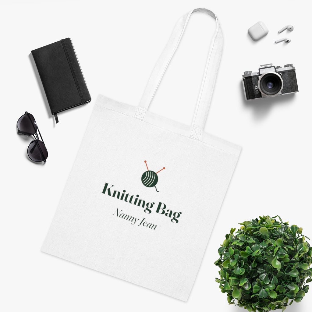 Personalised knitting tote bag mock-up laid flat beside a notebook, sunglasses, earphones, a camera and a plant