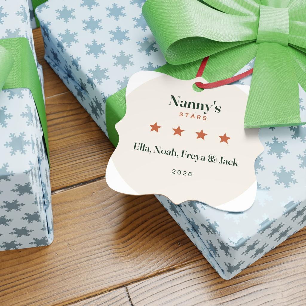 Personalised Nanny's Stars ornament mock-up resting on a snowflake-wrapped gift with a green bow on a wooden floor