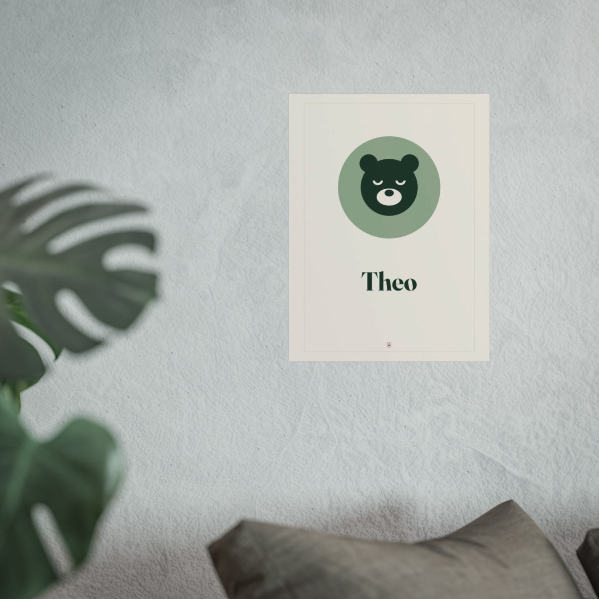 Nursery name print mock-up in the larger size on a grey wall above a sofa cushion, with a monstera leaf in front