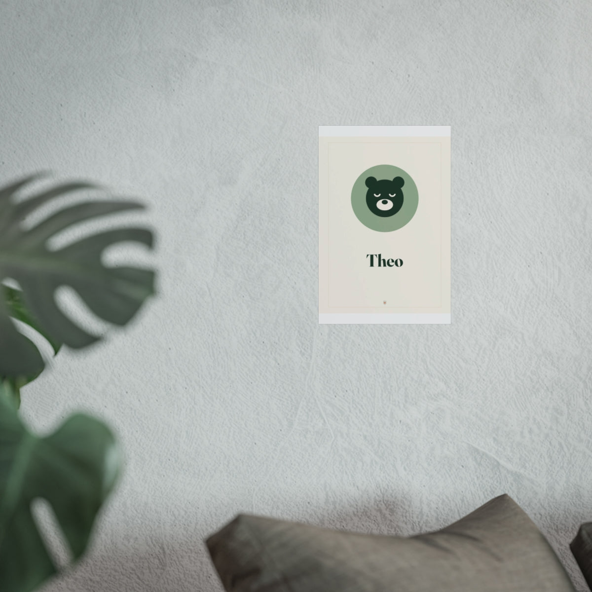 Nursery name print mock-up in the smaller size on the grey wall above a sofa cushion, bear and 'Theo' in green