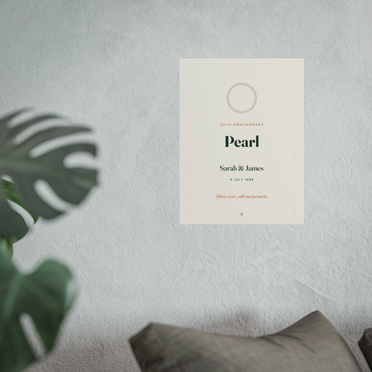 Pearl anniversary print mock-up in the larger size on a grey wall above a sofa cushion, with a monstera leaf in front