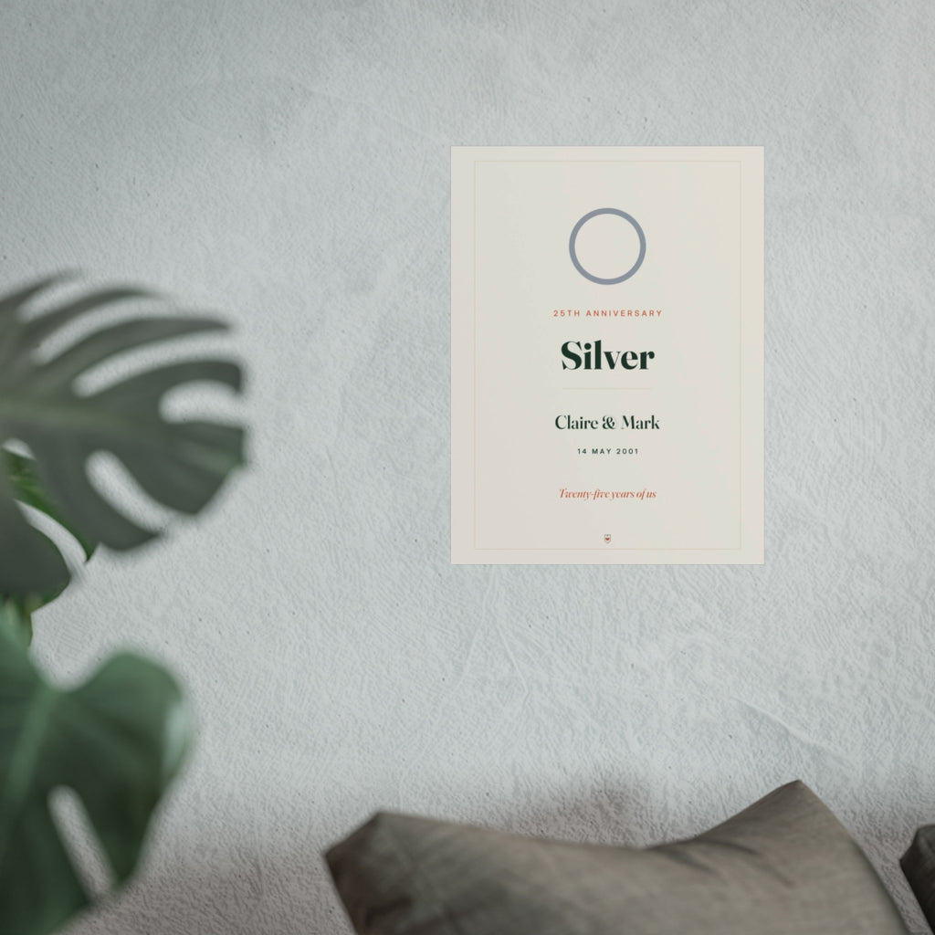 Silver anniversary print mock-up hung on a pale wall beside a monstera plant and a grey sofa, shown at the larger size