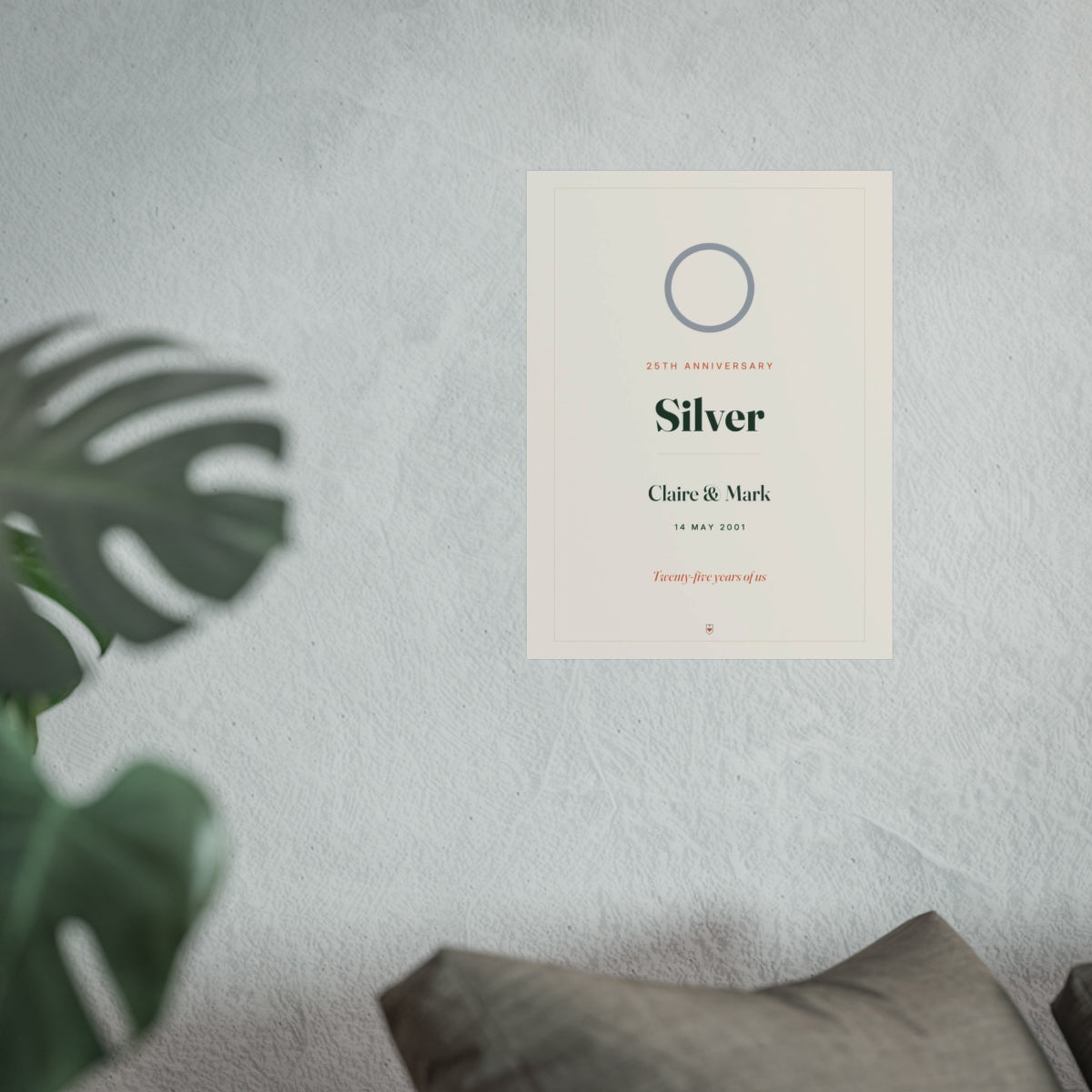 Silver anniversary print mock-up hung on a pale wall beside a monstera plant and a grey sofa, shown at the larger size
