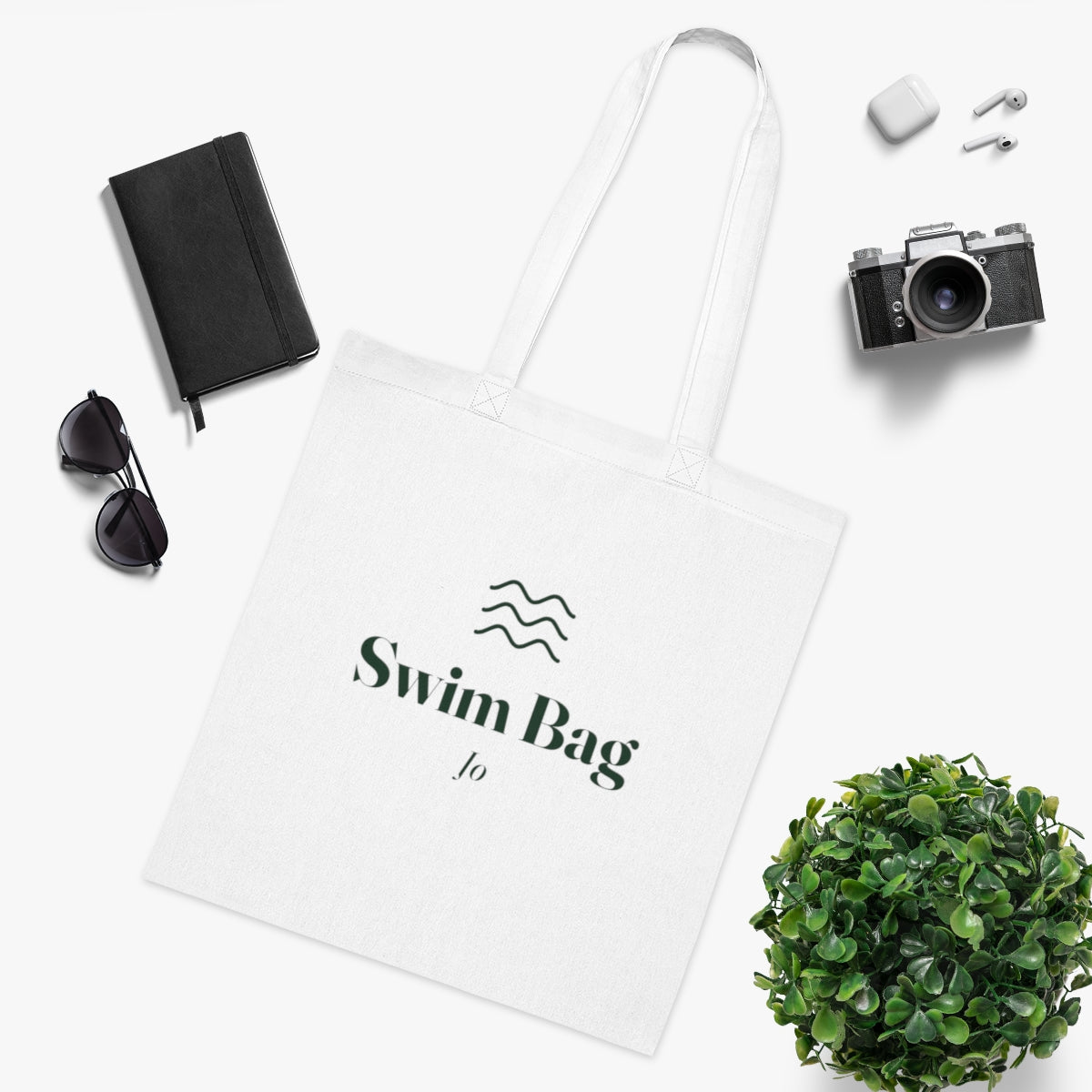 Swim bag tote mock-up in a flat lay with a notebook, sunglasses, camera, earbuds and a leafy plant